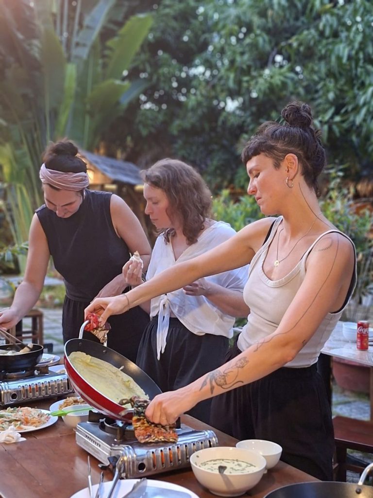 Three women cooking crispy pancakes on gas burners at an outdoor table.