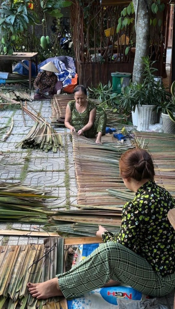 Local women sitting among stacks of leaves, weaving thatch panels.