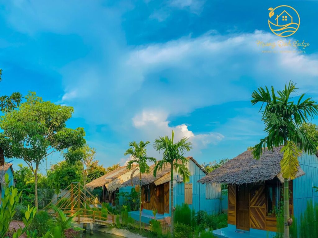 Thatched cottages with blue walls under a bright blue sky and palm trees.