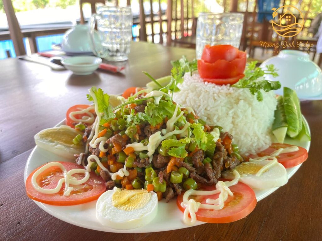 A plate of rice with diced stir-fried meat and vegetables, garnished with tomato and egg.