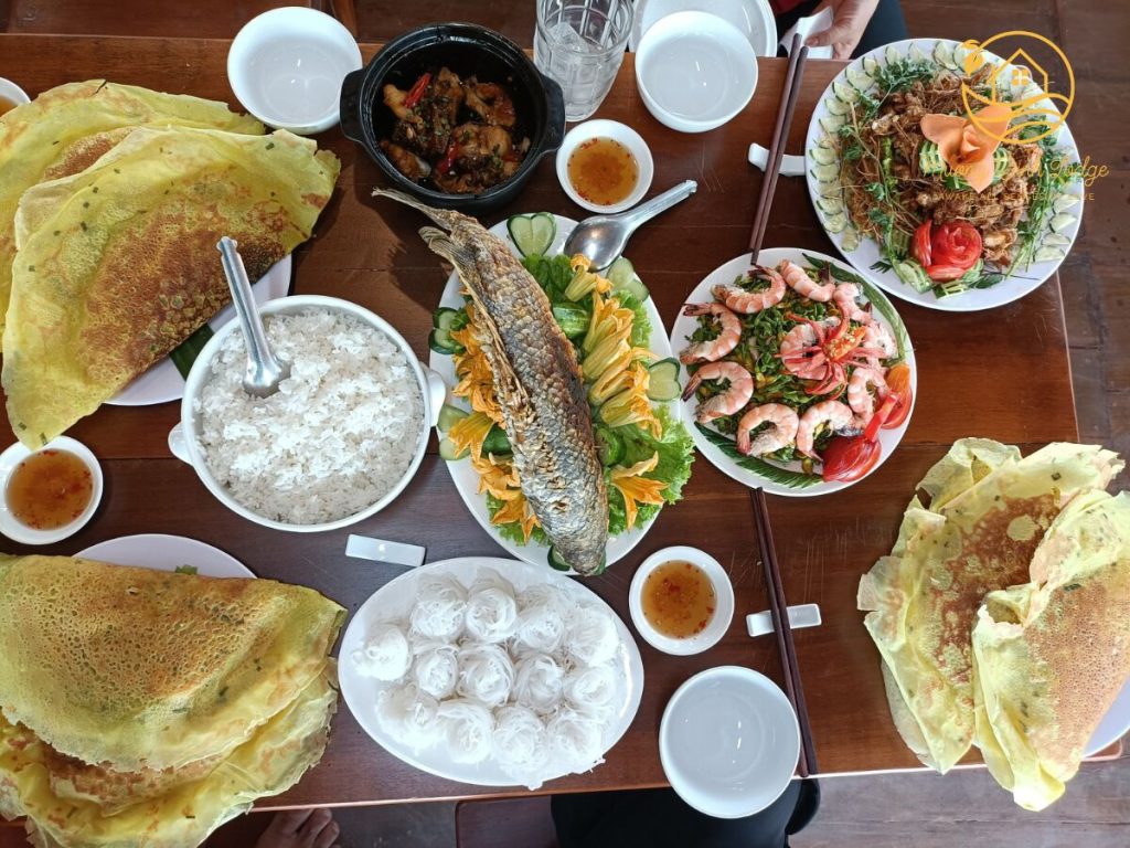 A table spread with crispy pancakes, grilled fish, prawns and a clay pot dish.