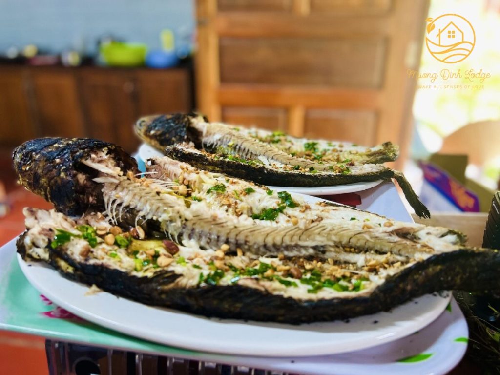 Two whole grilled fish topped with spring onions on white plates.