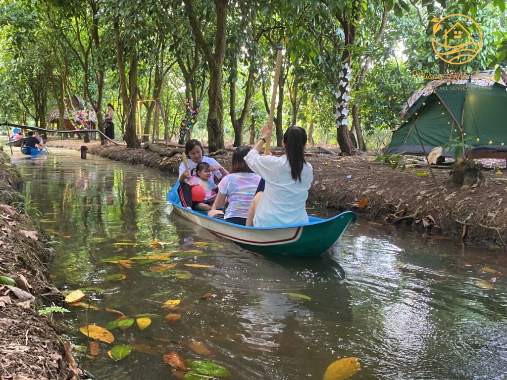 Guests in a small boat on a tree-lined canal, a tent pitched on the bank.