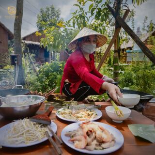 Cô đầu bếp đội nón lá chuẩn bị món ăn bên những đĩa tôm và giá.