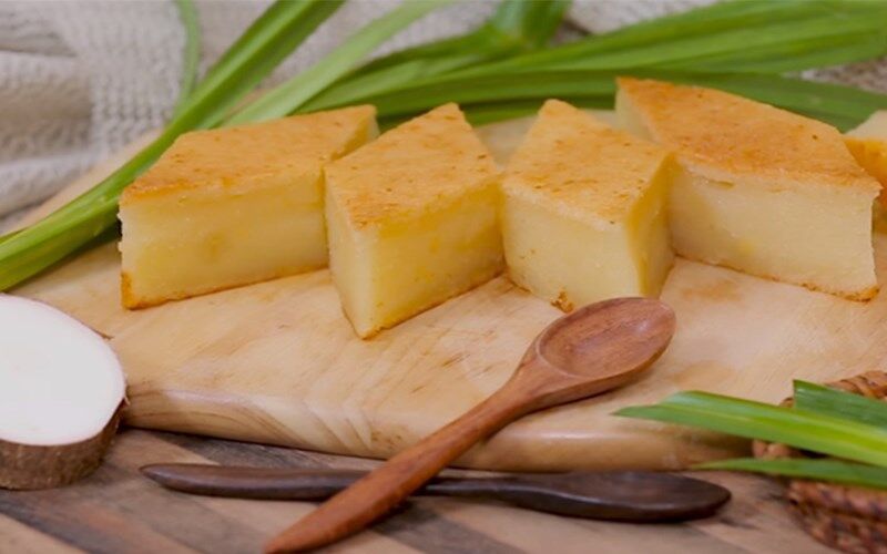 Squares of golden baked cake on a wooden board with green leaves and a wooden spoon.