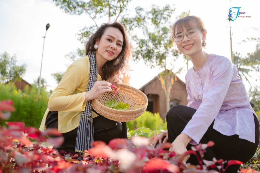 Two smiling women crouching among red-leaf plants with a basket of greens.