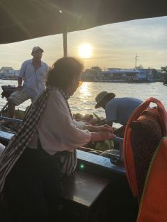 A woman in a checked scarf reaching across to a neighbouring boat, the sun low over the river.