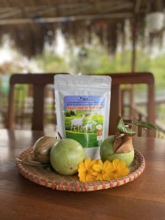 A pack of Ngọc Đào dried goat yogurt on a woven tray with green fruit and yellow flowers.