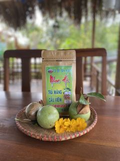 A pack of Nhan Ha soursop tea on a woven tray with green fruit and yellow flowers.