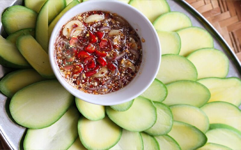 Slices of green mango around a bowl of chilli dipping sauce.