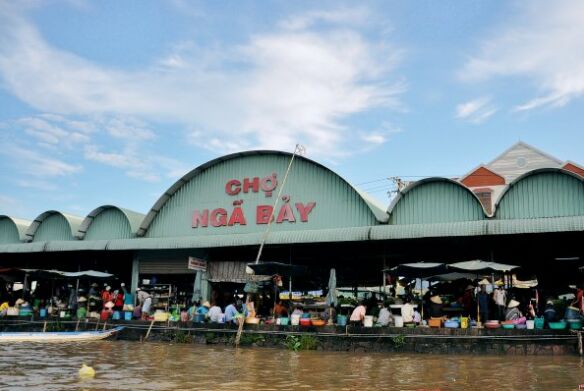 The arched hall of Ngã Bảy market beside the river, busy with shoppers.