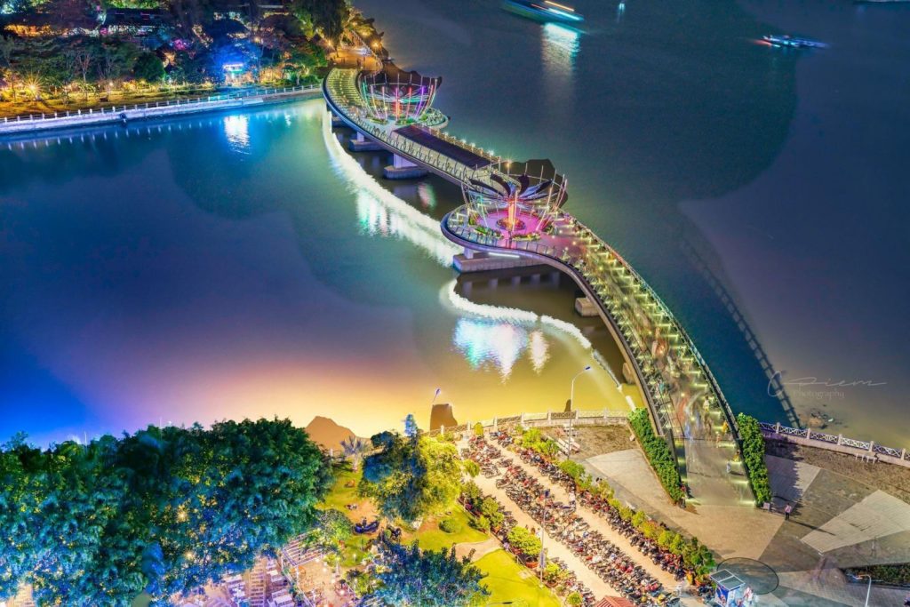 The Ninh Kieu pedestrian bridge lit up at night over the river, seen from above.