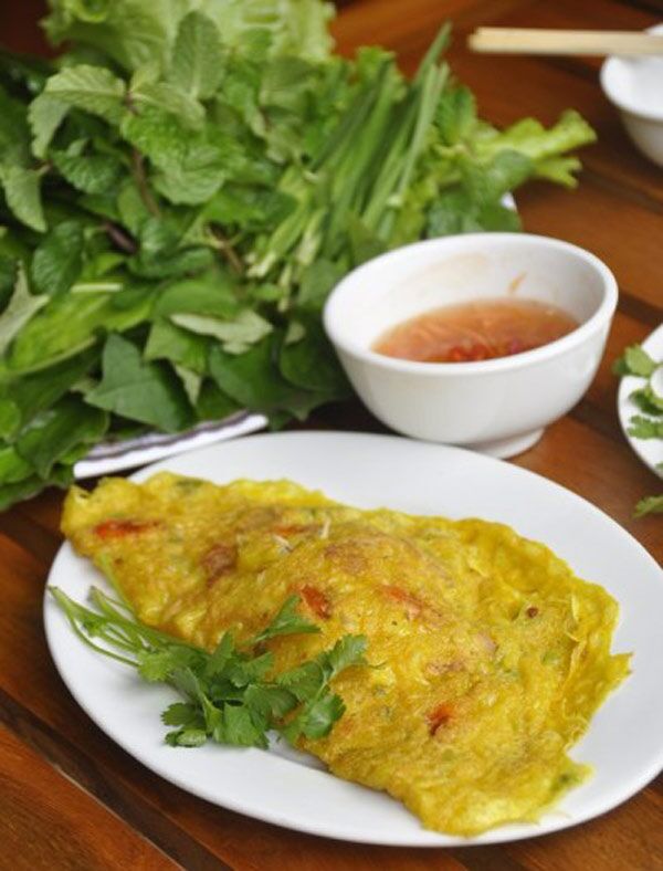A folded banh xeo on a plate with fresh herbs and dipping sauce.