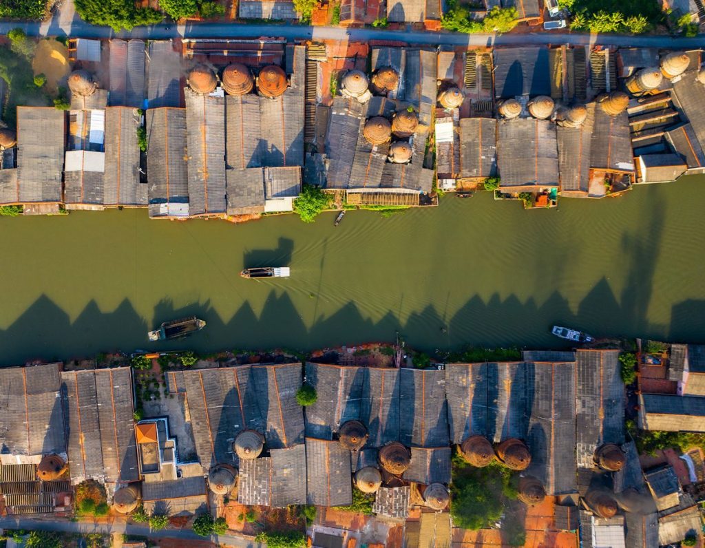 An aerial view of a canal lined with rows of rooftops and round kilns.