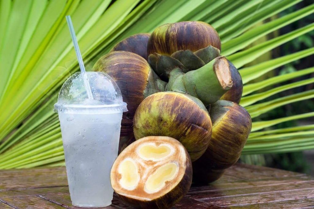 Sugar palm fruits, one cut open, beside a cup of iced drink.