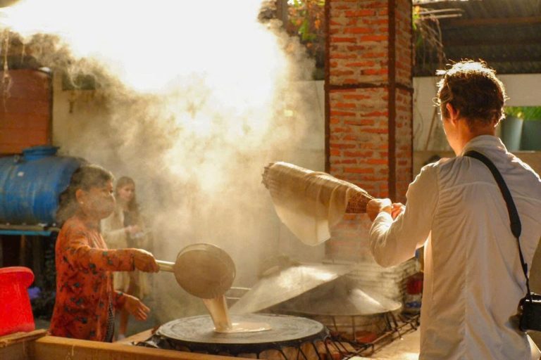 A woman spreading batter over a steaming pot as a visitor watches.