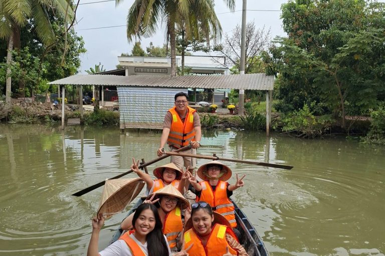 A family in orange life jackets and conical hats in a rowing boat on the canal.