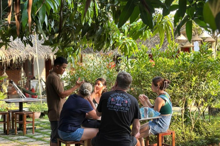 Guests chatting around outdoor tables in a garden beside thatched huts.