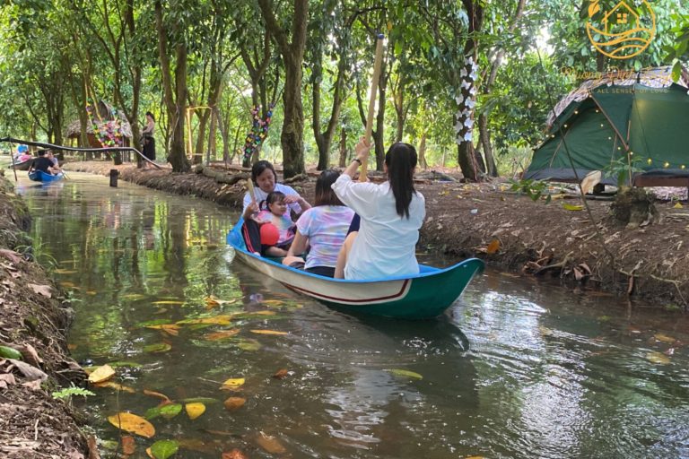 Guests in a small green boat on a tree-lined canal beside a tent.