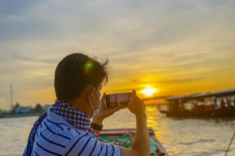 Người đàn ông trên ghe chụp ảnh mặt trời sát mặt sông.