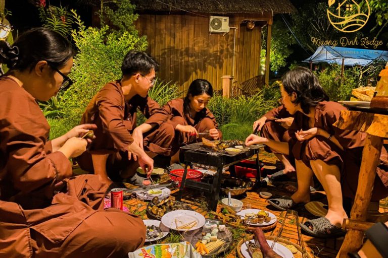 Guests in brown traditional outfits gathered around a grill at night.
