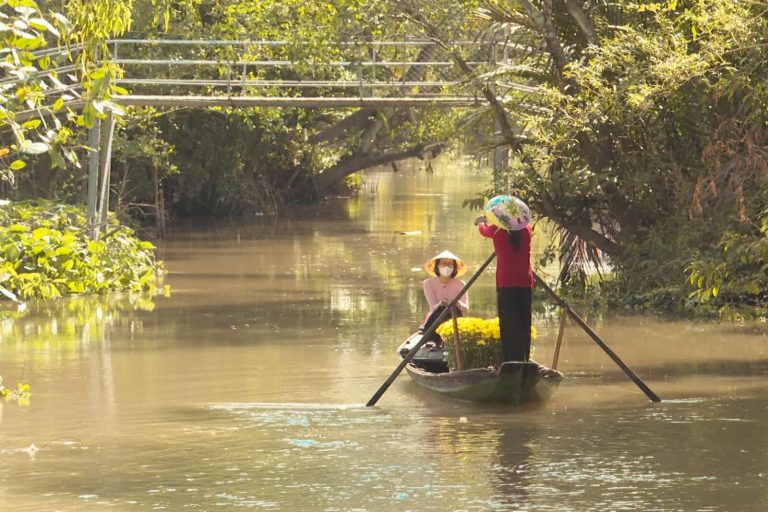 Two women rowing a small boat on a calm canal in warm evening light.