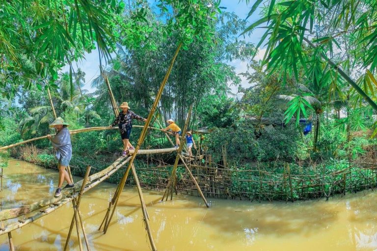 People crossing a bamboo monkey bridge over a brown canal.