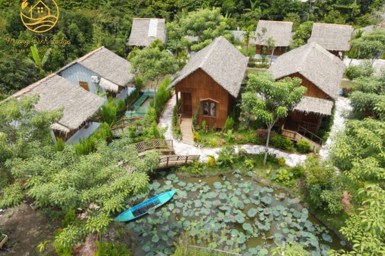 Aerial view of thatched cottages around a lotus pond with a small blue boat.