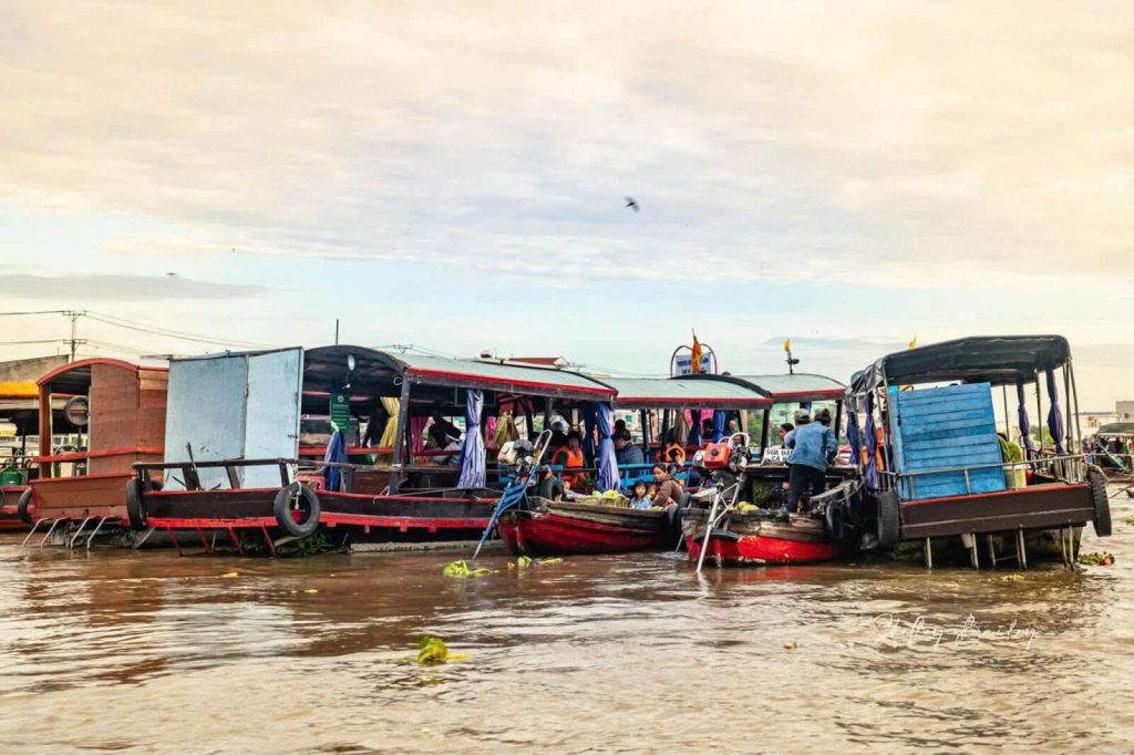 Wooden boats moored on a brown river with people on board.