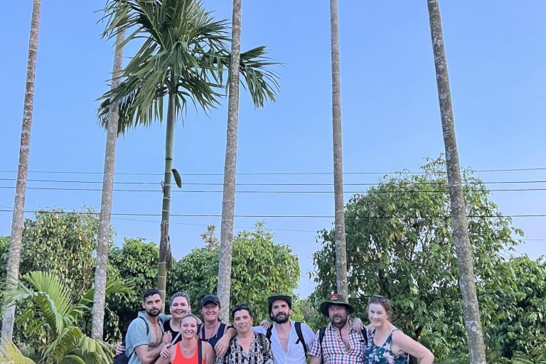 A group of travellers posing under tall areca palms.
