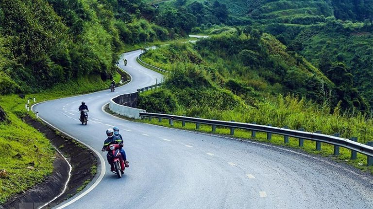 Motorbikes on a winding mountain road through green hills.