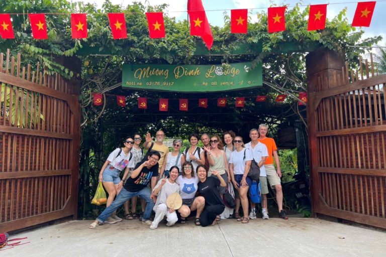 A large group of guests at the lodge's wooden gate under red flags and a Mương Đình Lodge sign.
