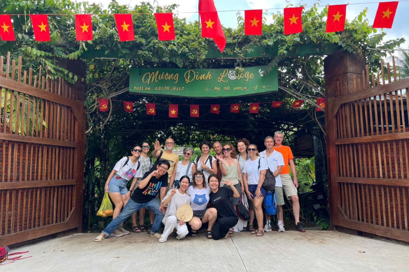 A large group of guests at the lodge's wooden gate under red flags and a Mương Đình Lodge sign.
