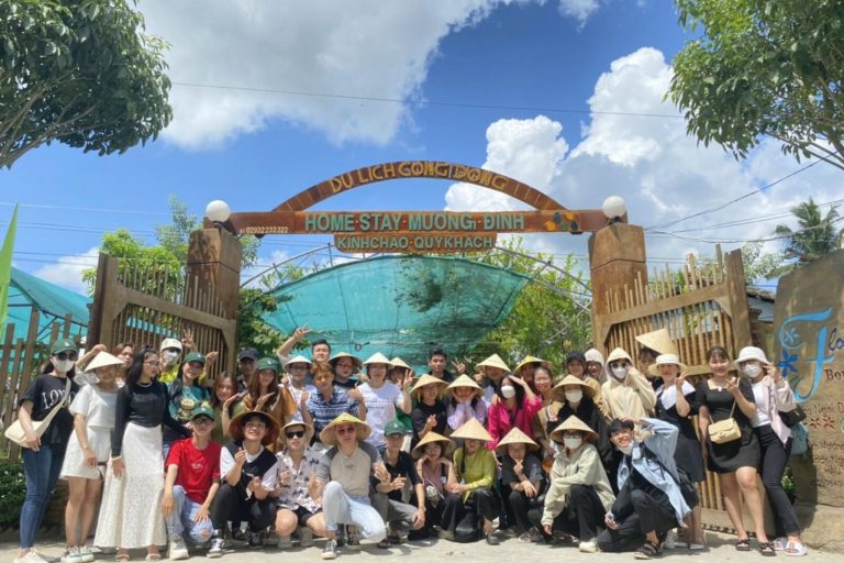 Đoàn người đông đội nón lá chụp chung dưới cổng vòm có bảng tên.