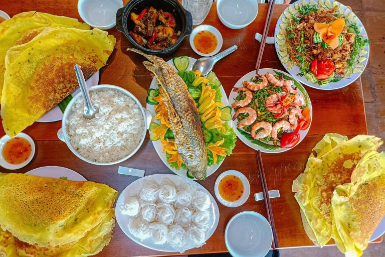 Mâm cơm với bánh vàng giòn, cá nướng nguyên con, tôm và những chiếc bánh trắng nhỏ.