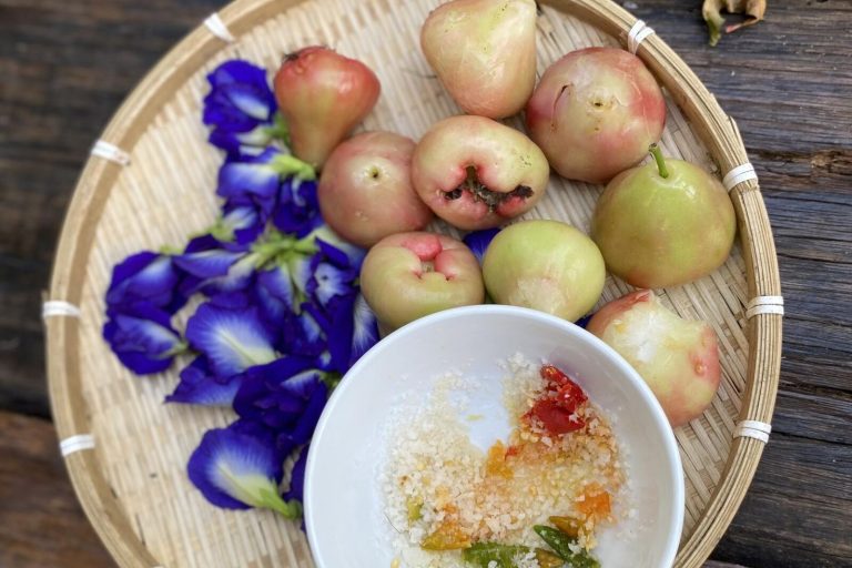 Pink and green fruit with blue flowers on a woven tray, beside a bowl of chilli salt.