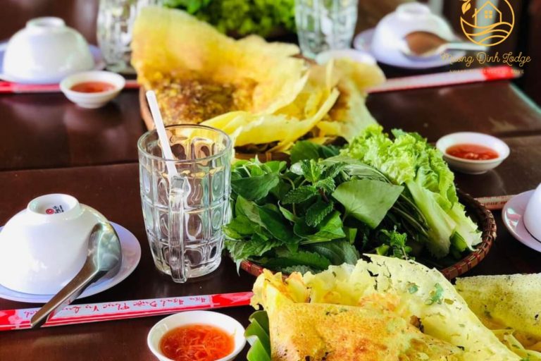 Bánh xèo pancakes with fresh greens and dipping sauce on a table, with the lodge logo.
