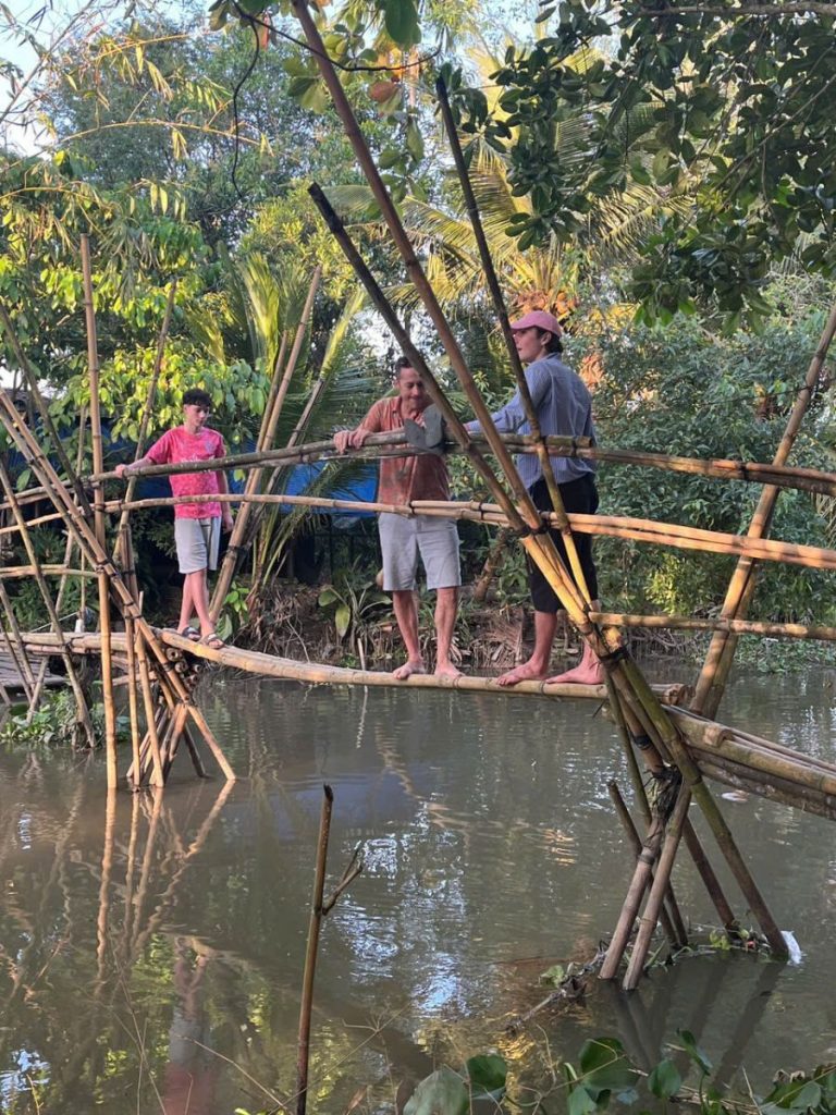 Guests crossing a bamboo monkey bridge over a canal.