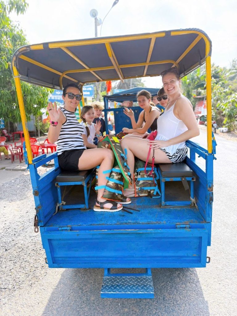 Guests riding on the back of a blue open motor cart along a road.