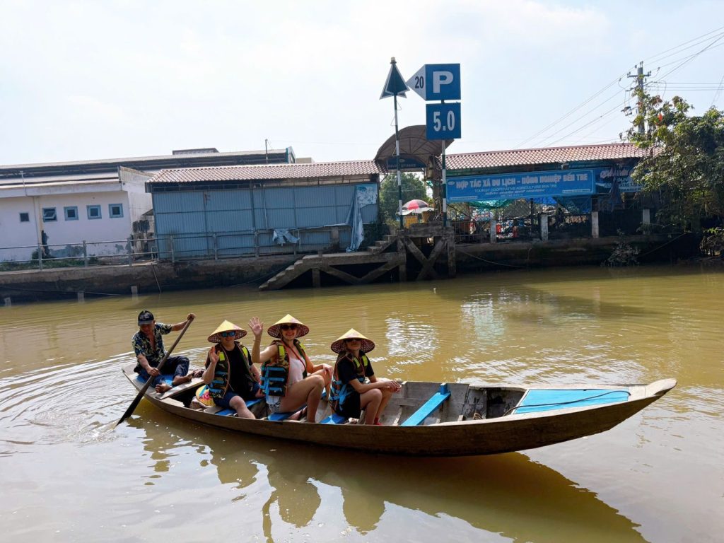 Guests in conical hats rowed in a long wooden boat on a brown river.