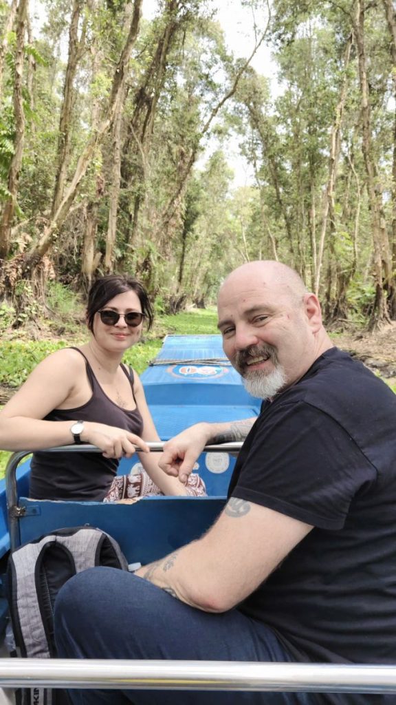 Two guests in a small boat among the tall thin trees of a cajuput forest.