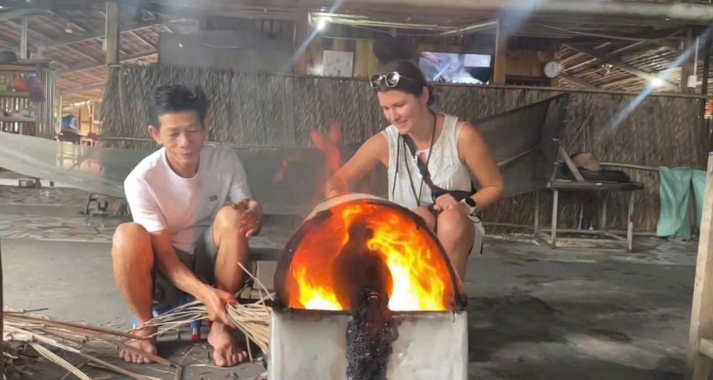 A guest and a local man squatting beside a round stove with a roaring fire.