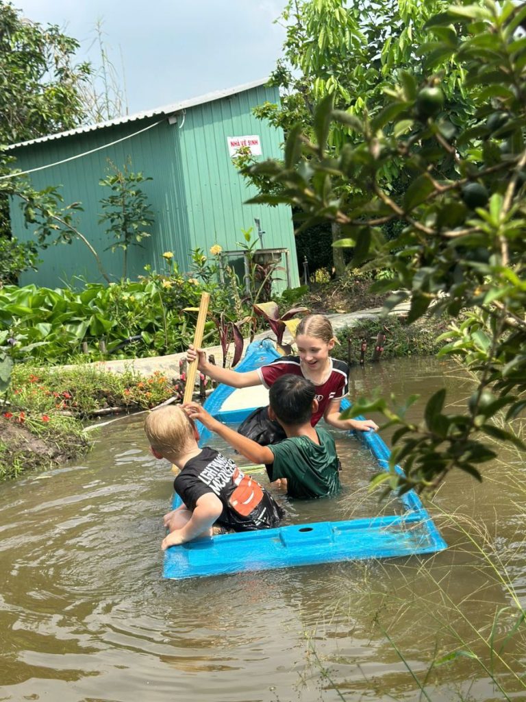 Children paddling a blue plastic raft along a canal.