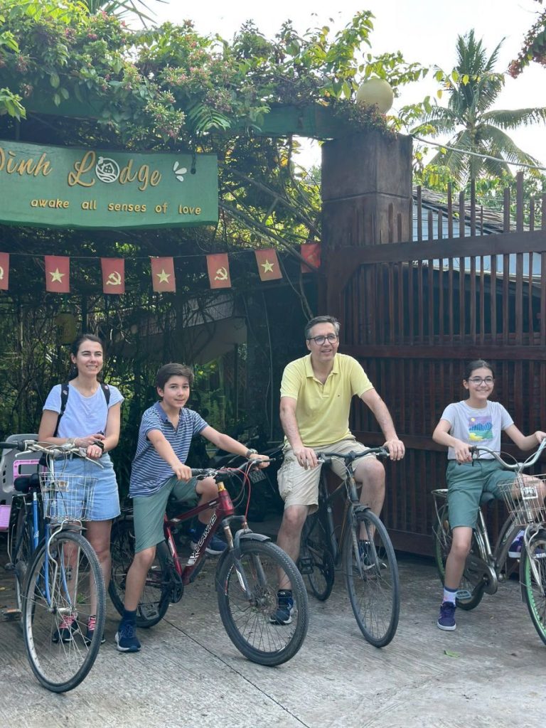 A family on bicycles in front of the lodge gate hung with red flags.
