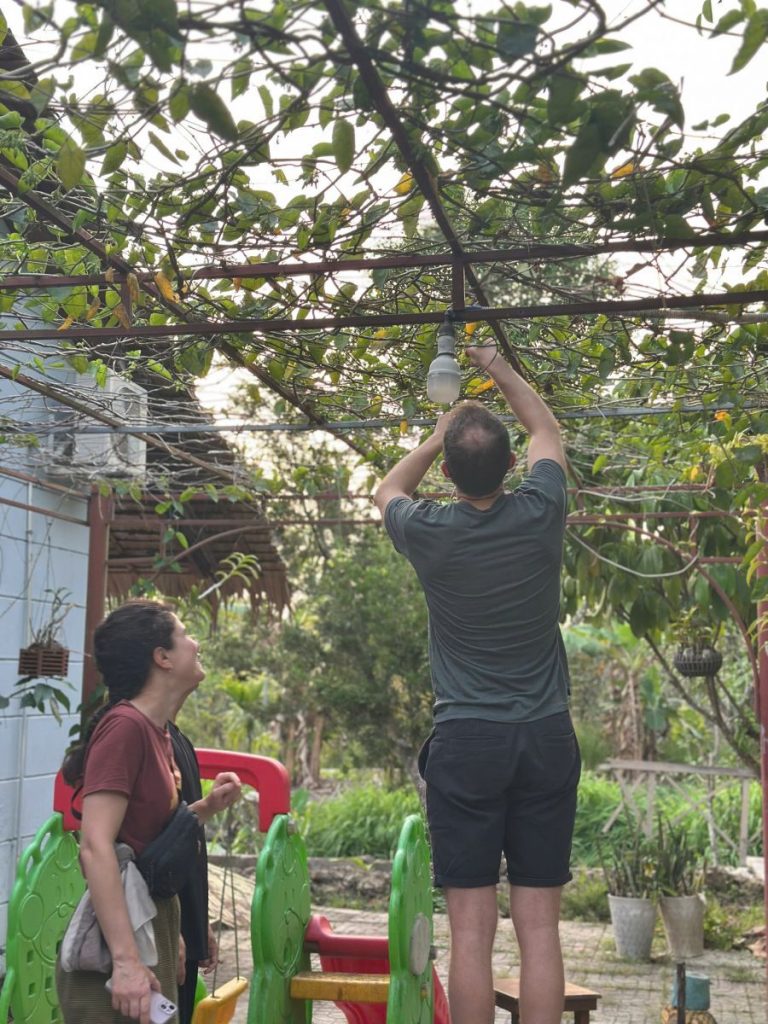 A guest reaching up into a fruit tree as a woman watches beside a garden slide.