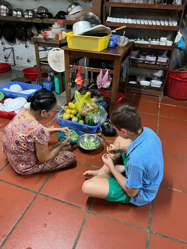 A woman and a boy sitting on a tiled kitchen floor preparing vegetables.