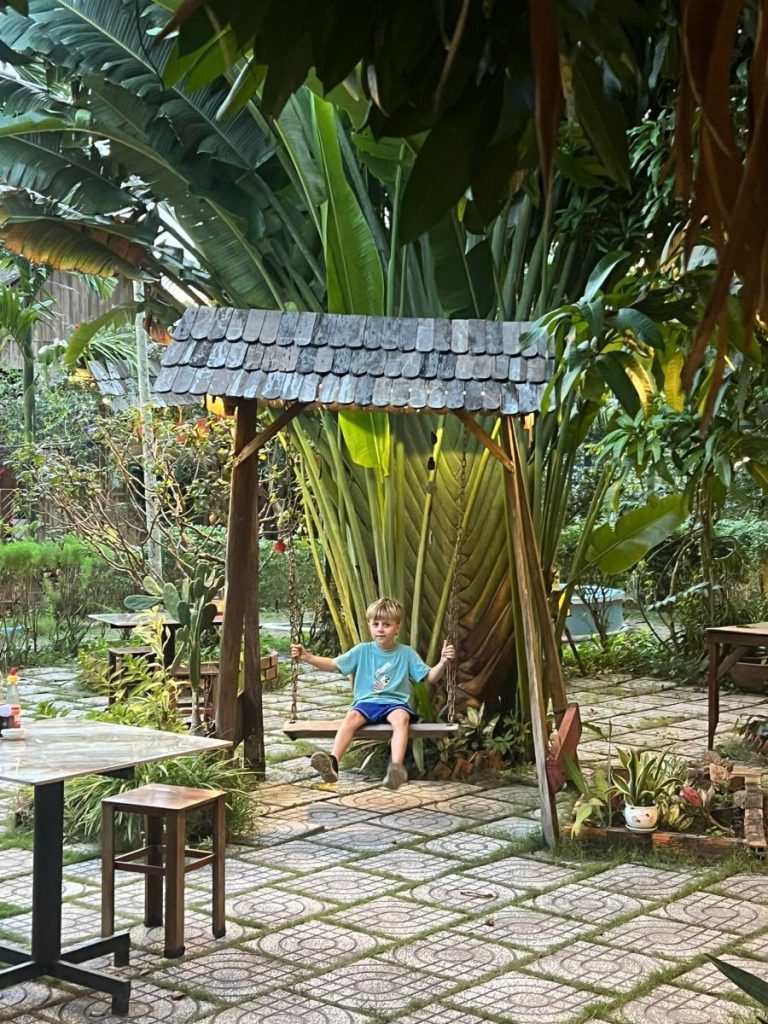 A child on a wooden swing with a shingled roof in a garden courtyard.