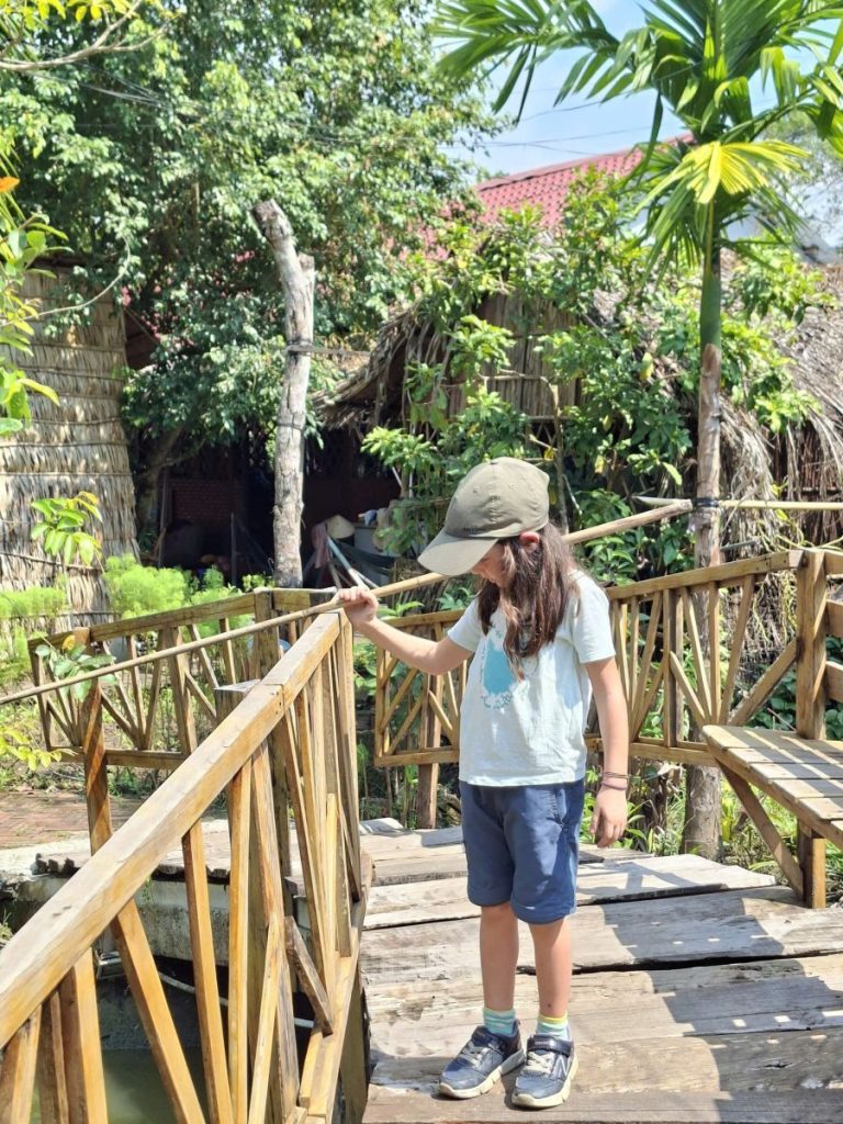A girl in a cap walking along a wooden bridge in the garden.