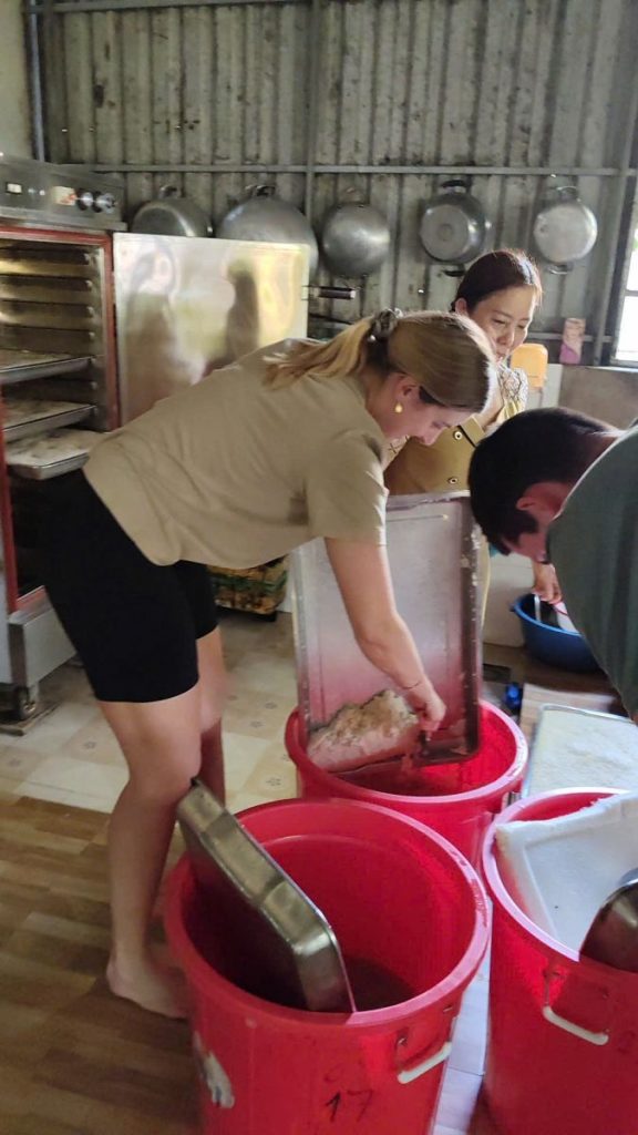 A visitor bending over red buckets beside a steel cooker in a workshop.