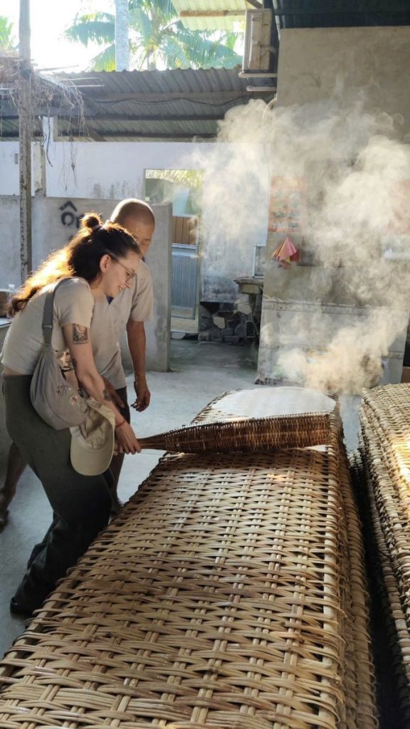 Two visitors watching steam rise over woven bamboo drying racks.